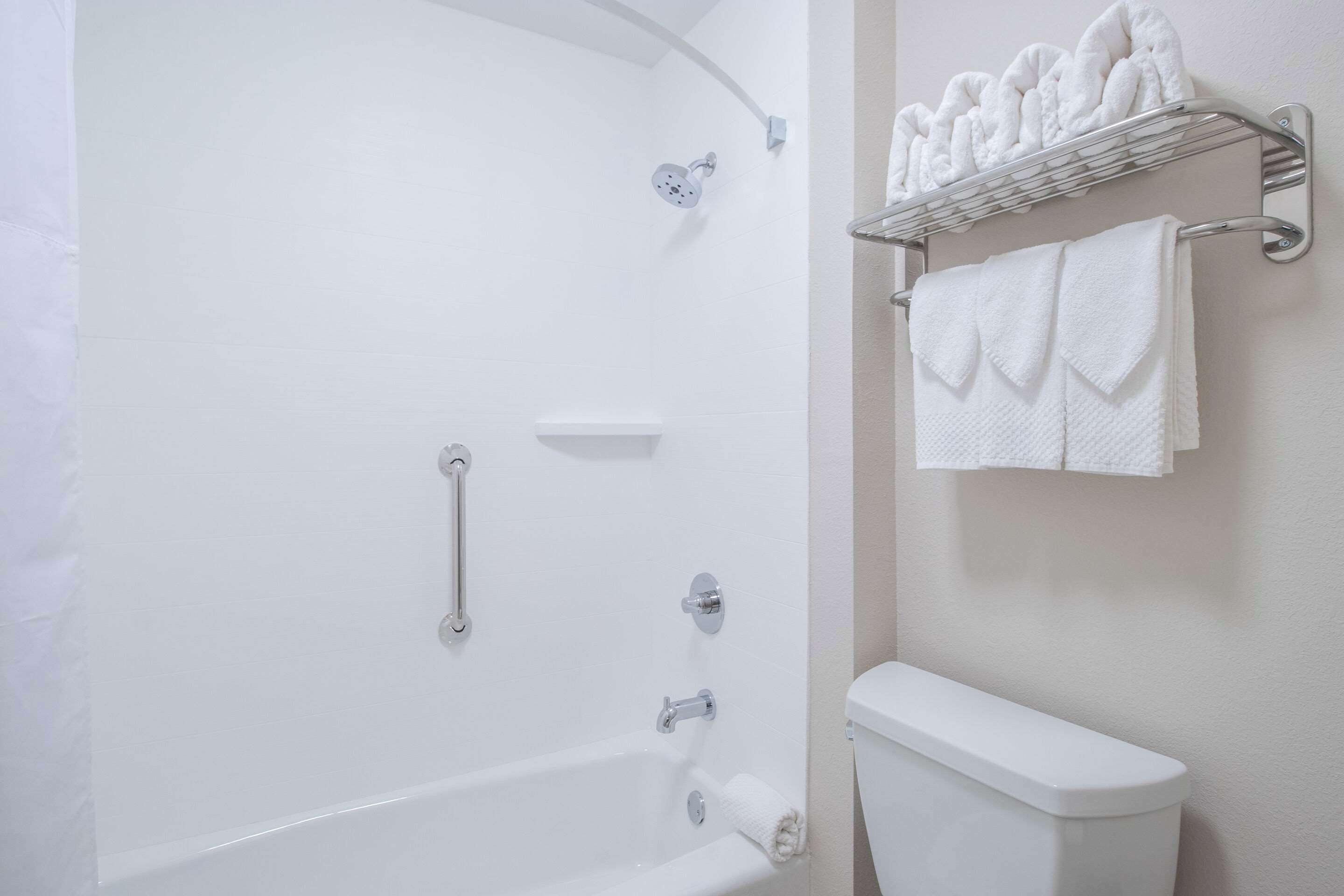 A bathroom with a bathtub, a toilet, a showerhead, a towel rack with towels, and a shelf with toiletries.