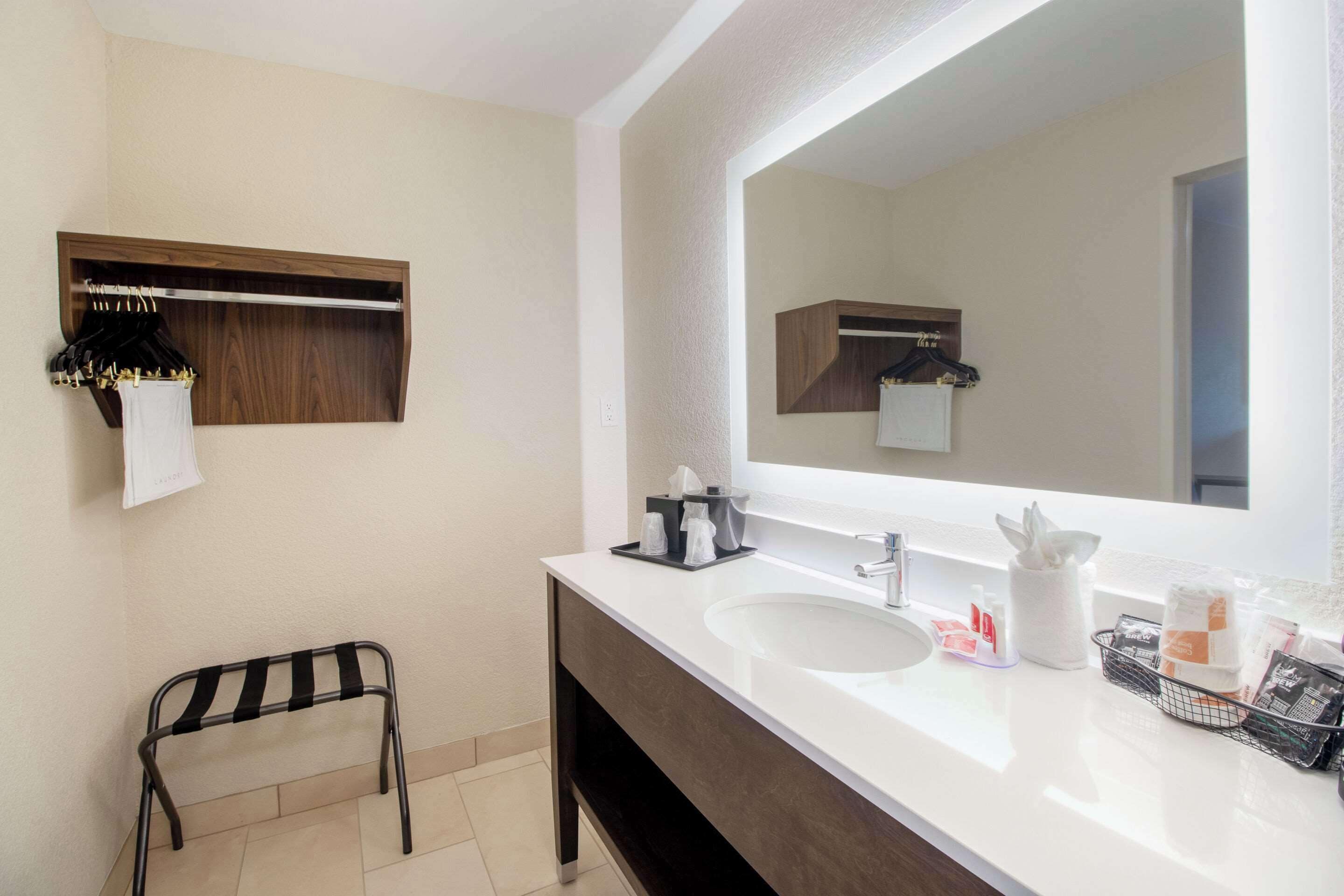 A bathroom with a large mirror, a sink, a towel rack, and a small stool.