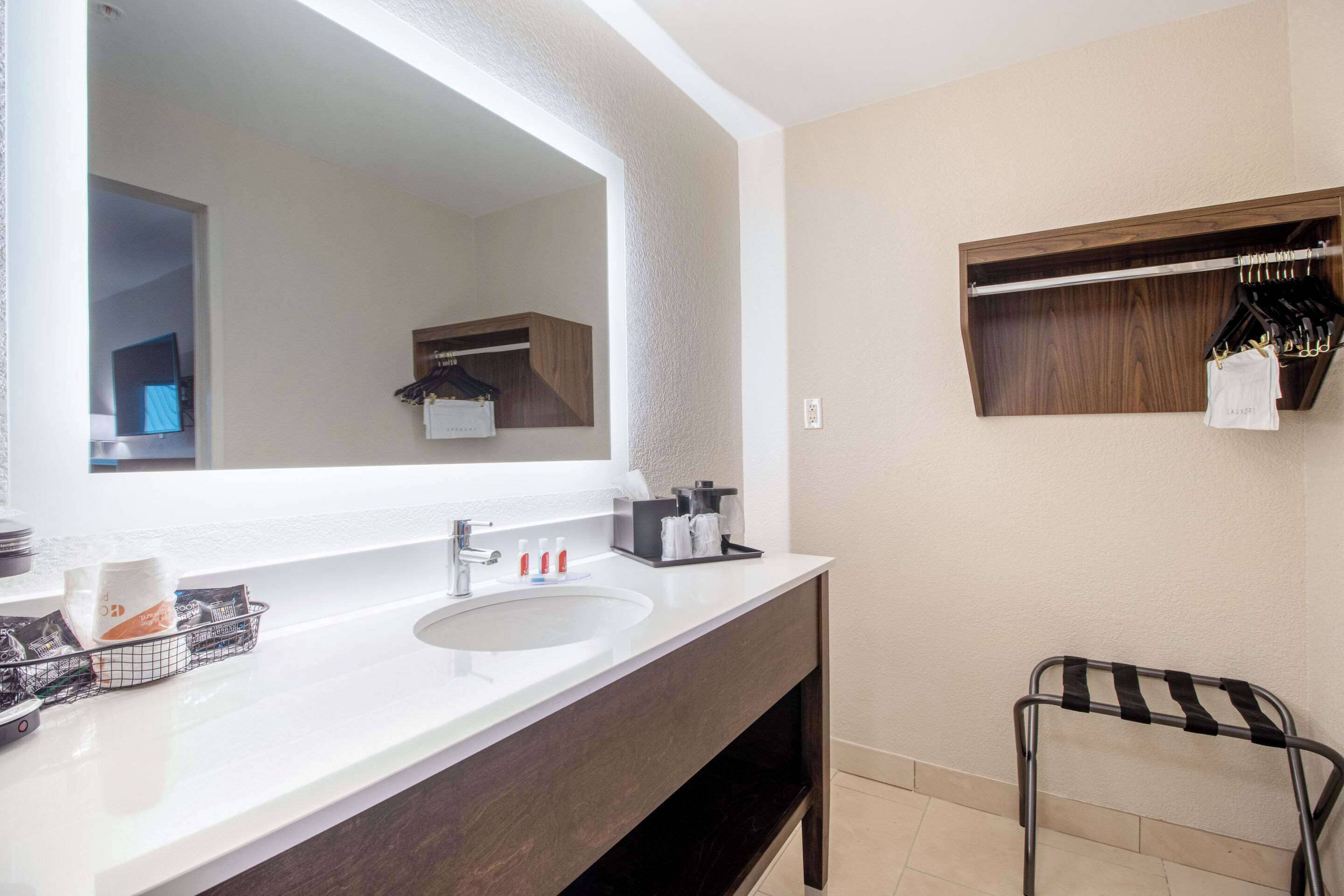 A modern bathroom with a large mirror, a sink, a towel rack, and a small shelf with toiletries.