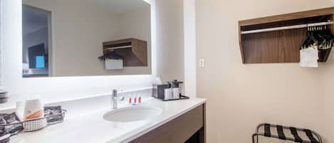 A modern bathroom with a large mirror, a sink, a towel rack, and a small shelf with toiletries.