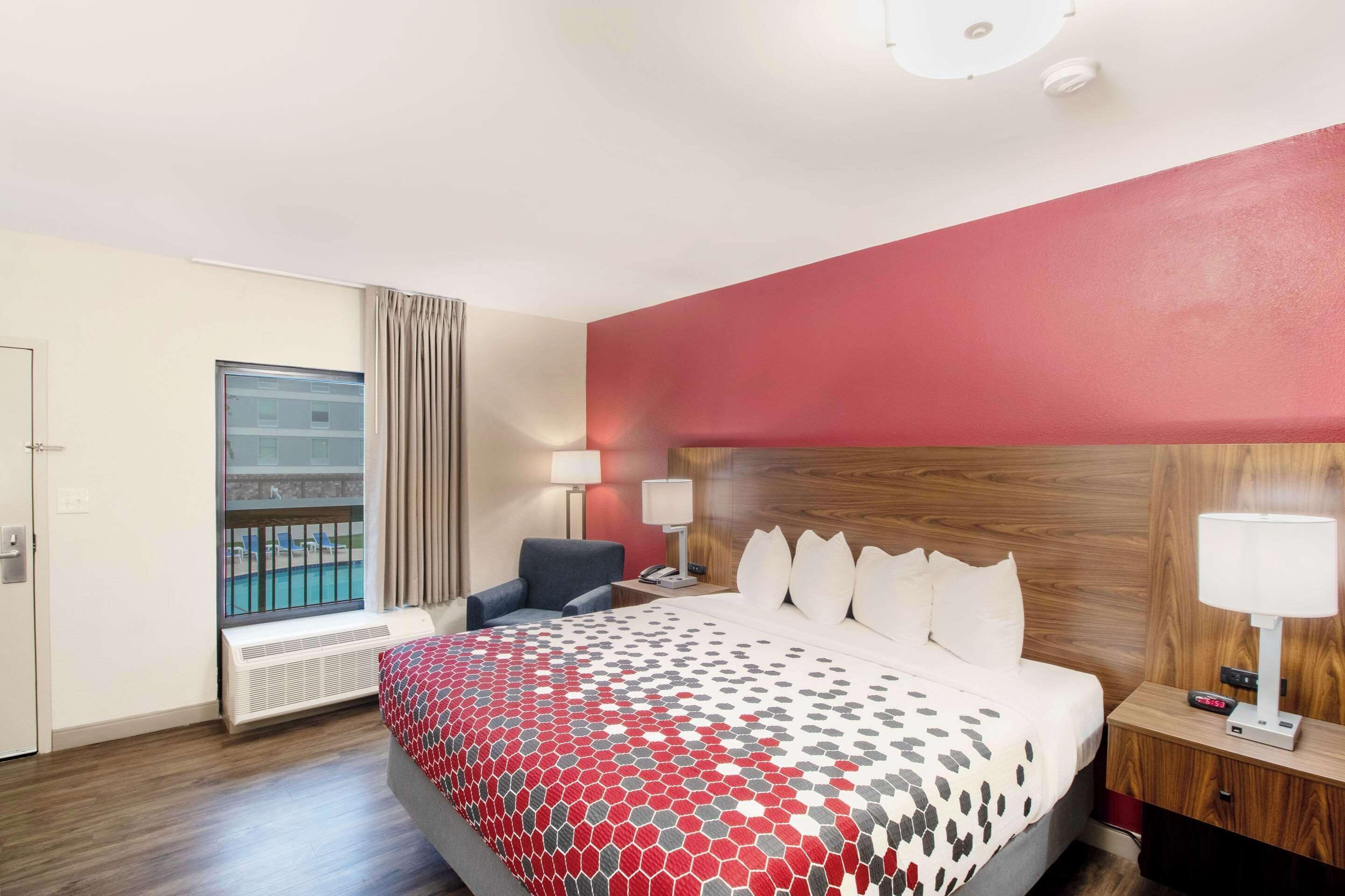 Una habitación de hotel con una cama grande, una silla, una mesita de noche, una lámpara y una ventana con vistas a una piscina.