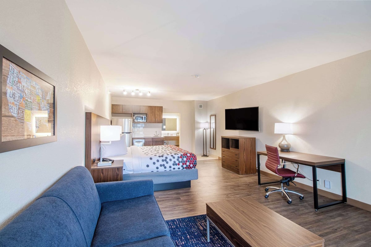 Een moderne hotelkamer met een bed, een bureau, een stoel, een bank, een televisie en een keuken in de achtergrond.