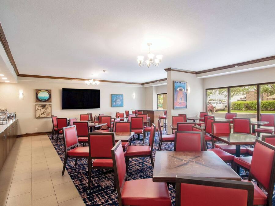 Une salle à manger d'hôtel avec des chaises et des tables rouges, un téléviseur à écran plat fixé au mur et une vue sur l'extérieur grâce à de grandes fenêtres.