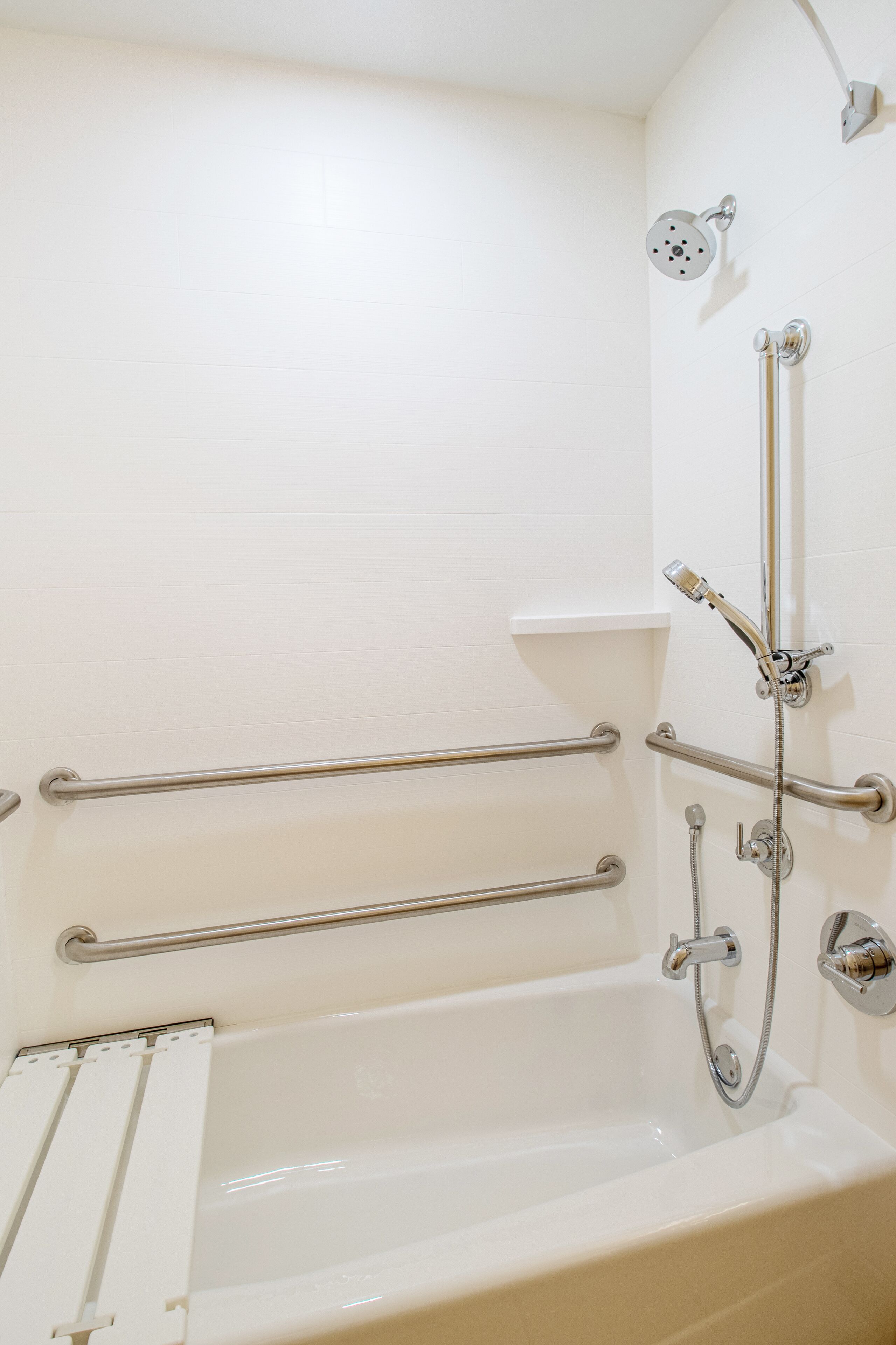 Une baignoire équipée de barres d’appui, d’un pommeau de douche et d’un flexible de douche.