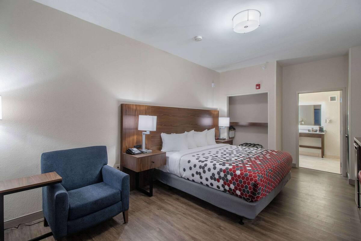 Een hotelkamer met een bed, een bureau, een stoel en een nachtkastje met een lamp.