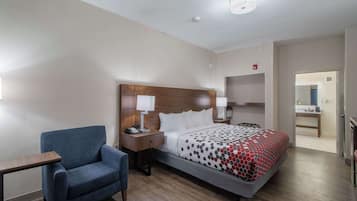 A hotel room with a bed, a desk, a chair, and a nightstand with a lamp.