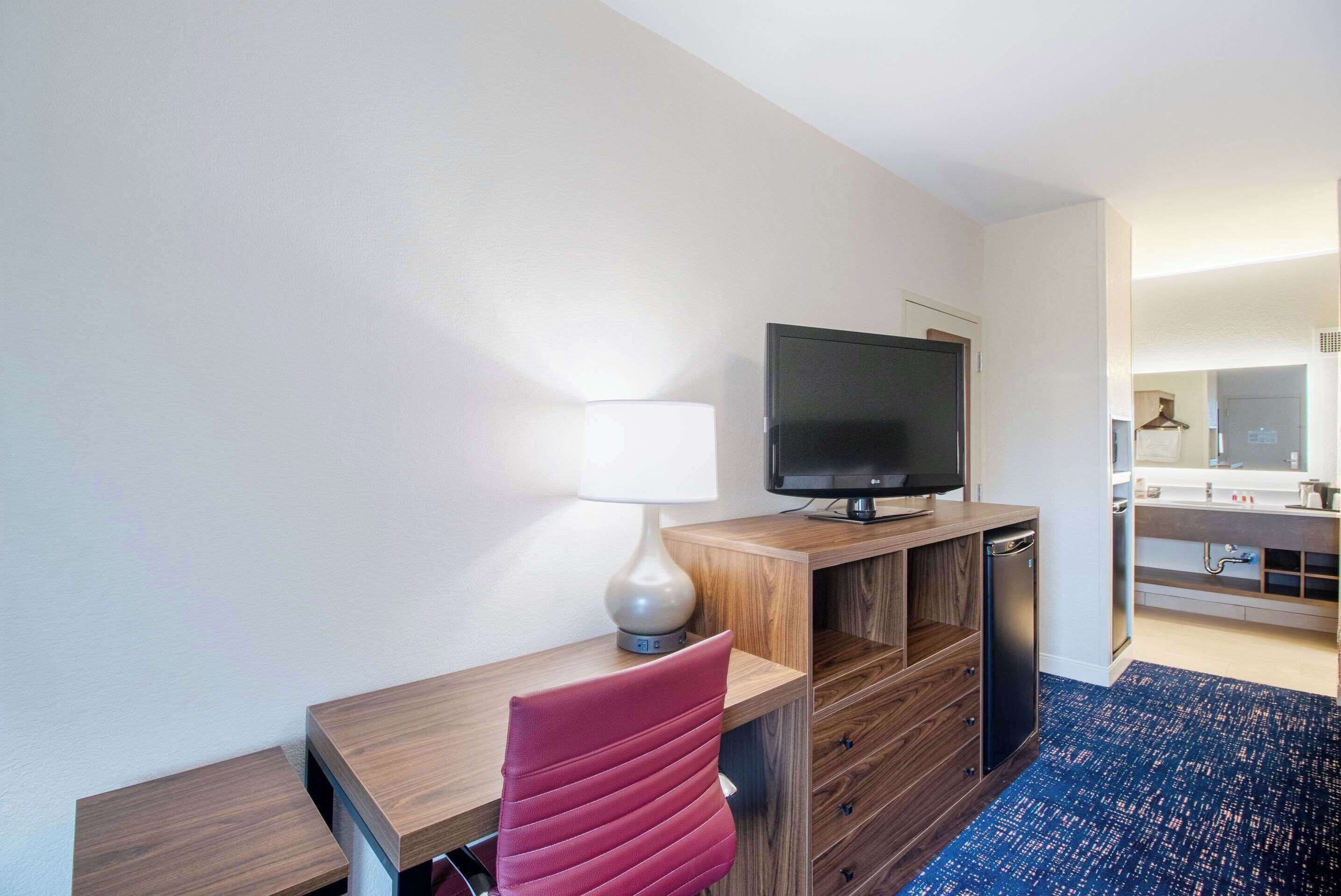 A hotel room with a wooden desk, a television, a lamp, and a blue carpet.