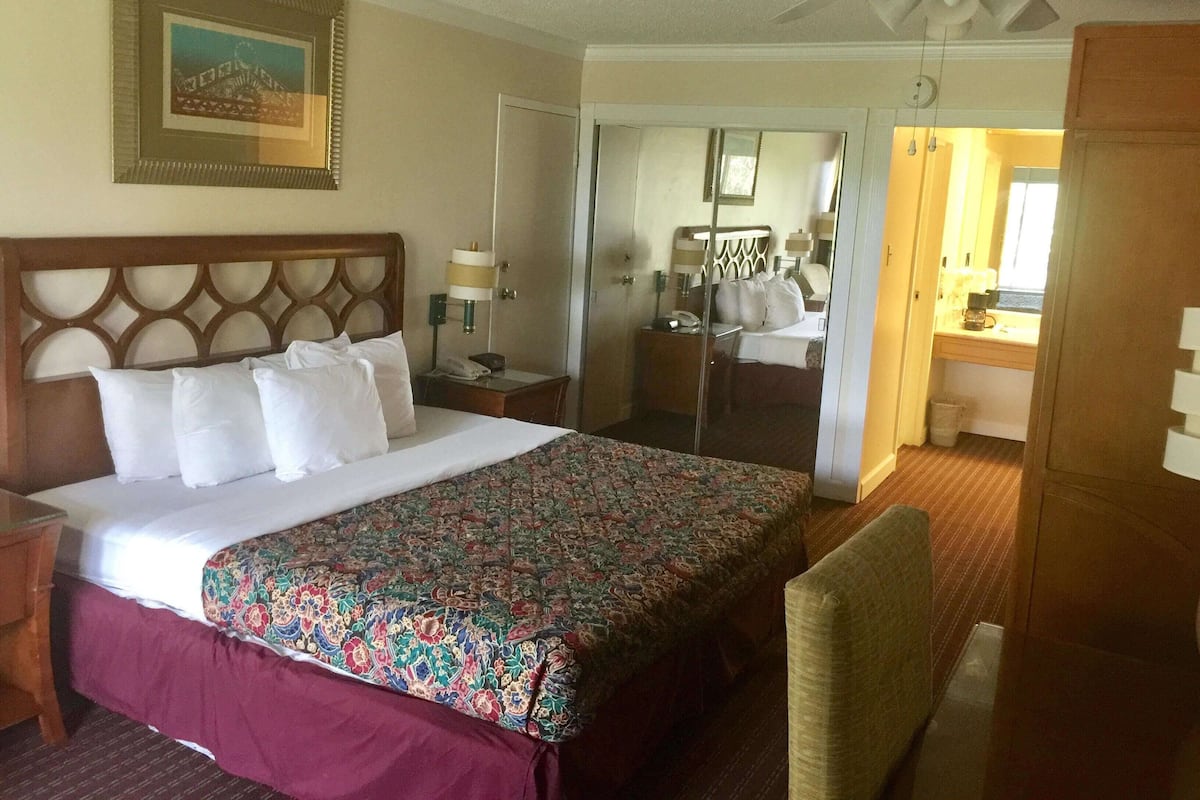 A hotel room with a bed, a nightstand, a chair, a ceiling fan, a bathroom with a shower, and a mirror.