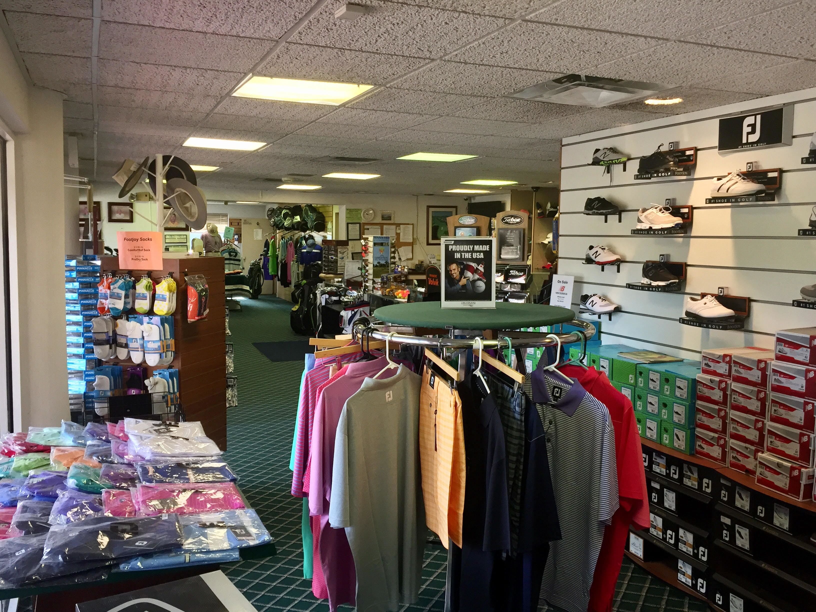 A retail store with shelves of golf shoes and socks, a rack of clothing, and a display of colorful bags.