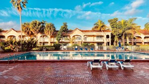 A hotel pool area with a clear blue sky, palm trees, and a brick patio with lounge chairs. - Grand Palms Spa & Golf Resort (Pembroke Pines)