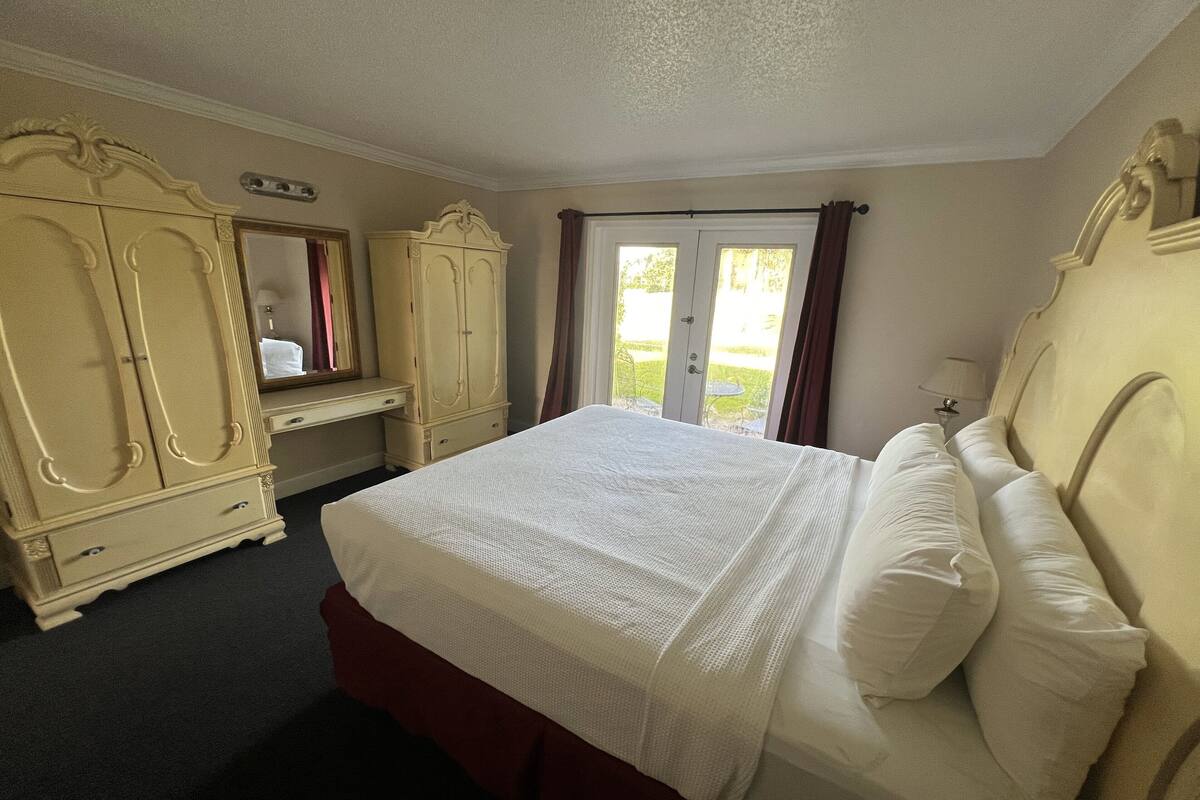 A bedroom with a large bed, a wardrobe, a mirror, and a window with curtains.