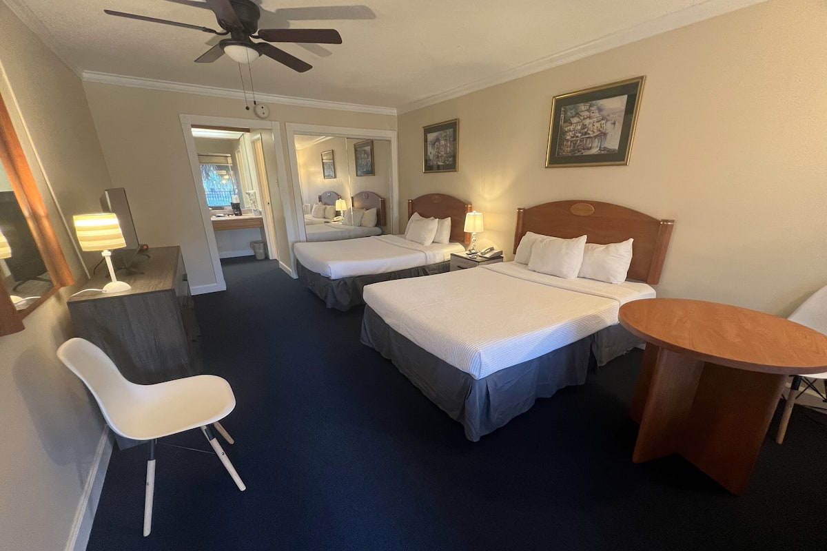 A hotel room with two beds, a desk, a chair, and a small table.