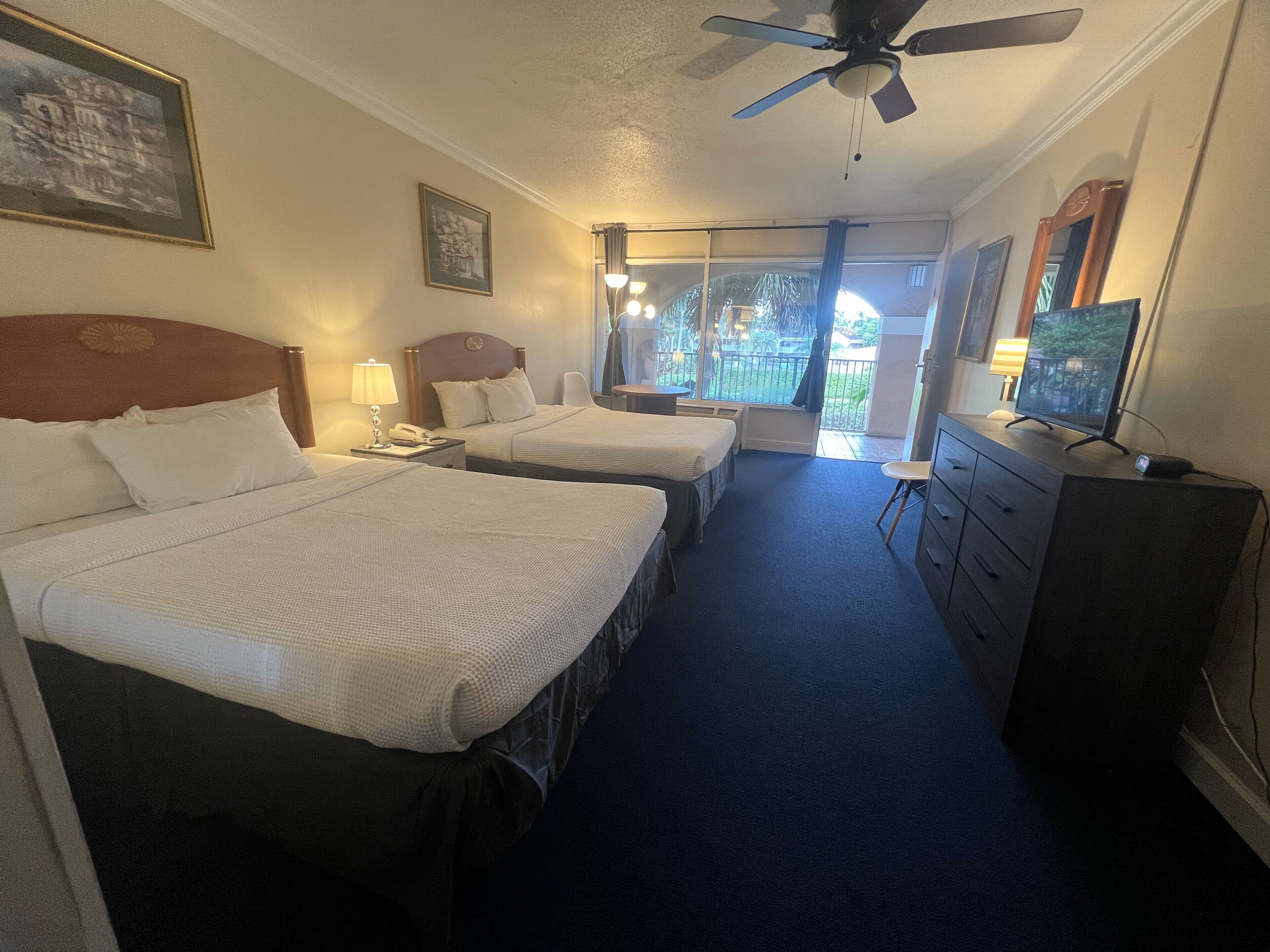 Hotelkamer met twee bedden, een plafondventilator, een televisie en uitzicht op de omgeving.