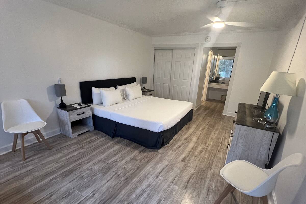 A bedroom with a bed, two bedside tables, a chair, a desk, and a ceiling fan.