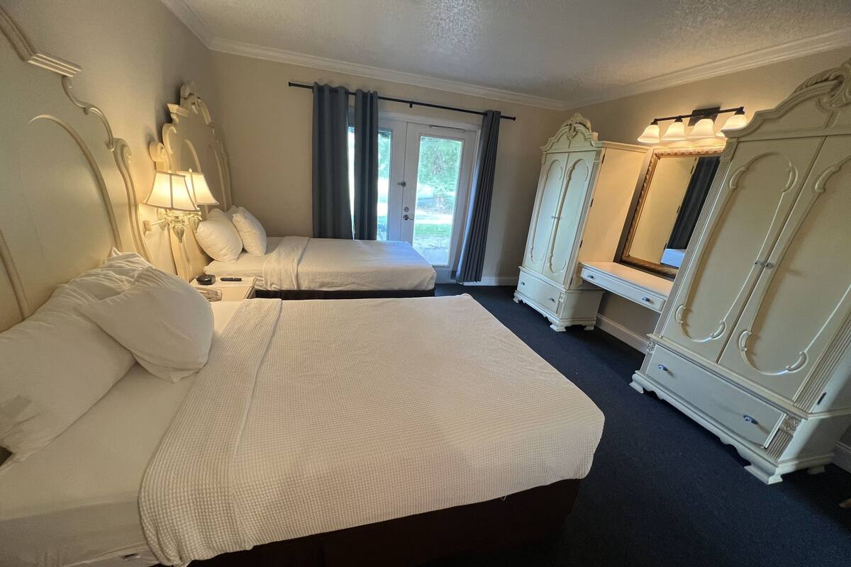 A hotel room with two beds, a large mirror, a wardrobe, and a window with curtains.