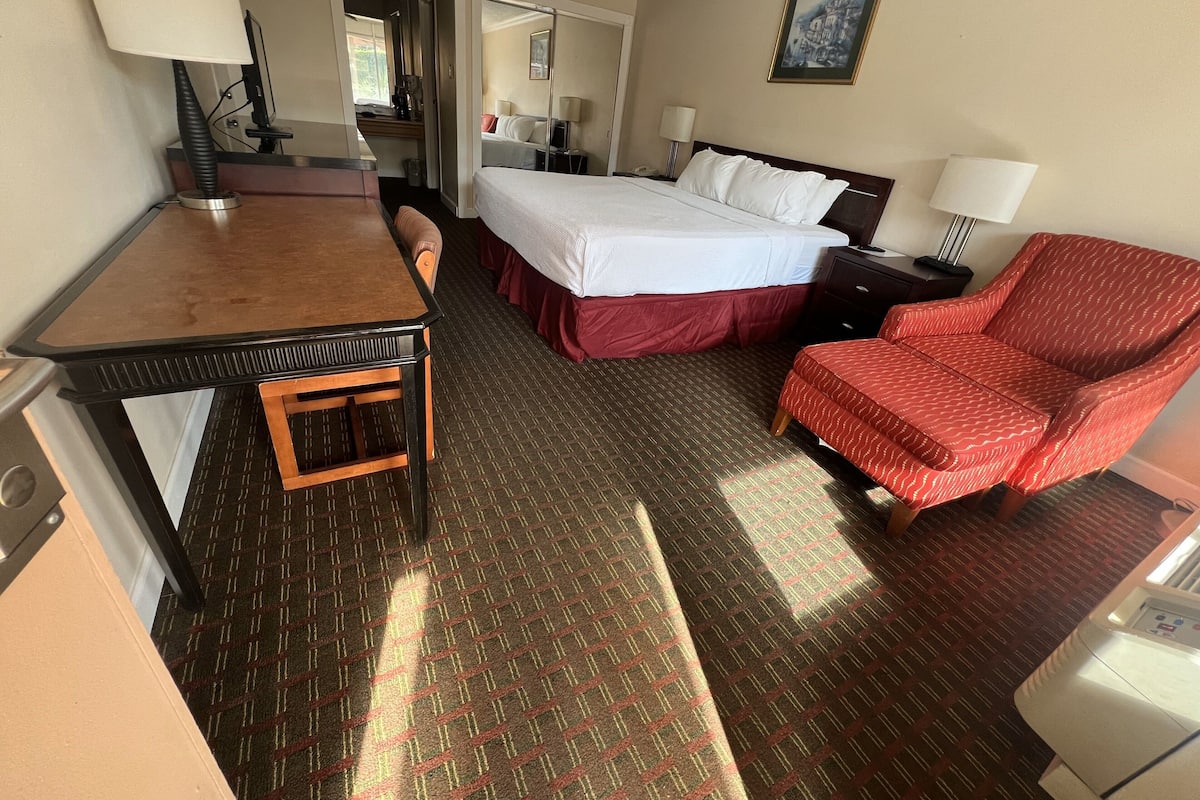 A hotel room with a bed, a desk, a chair, a nightstand, and a lamp.