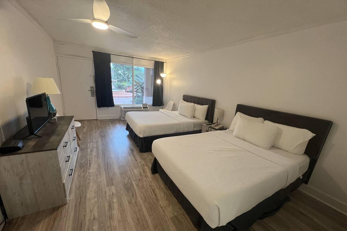 A hotel room with two beds, a desk with a computer, and a window with curtains.