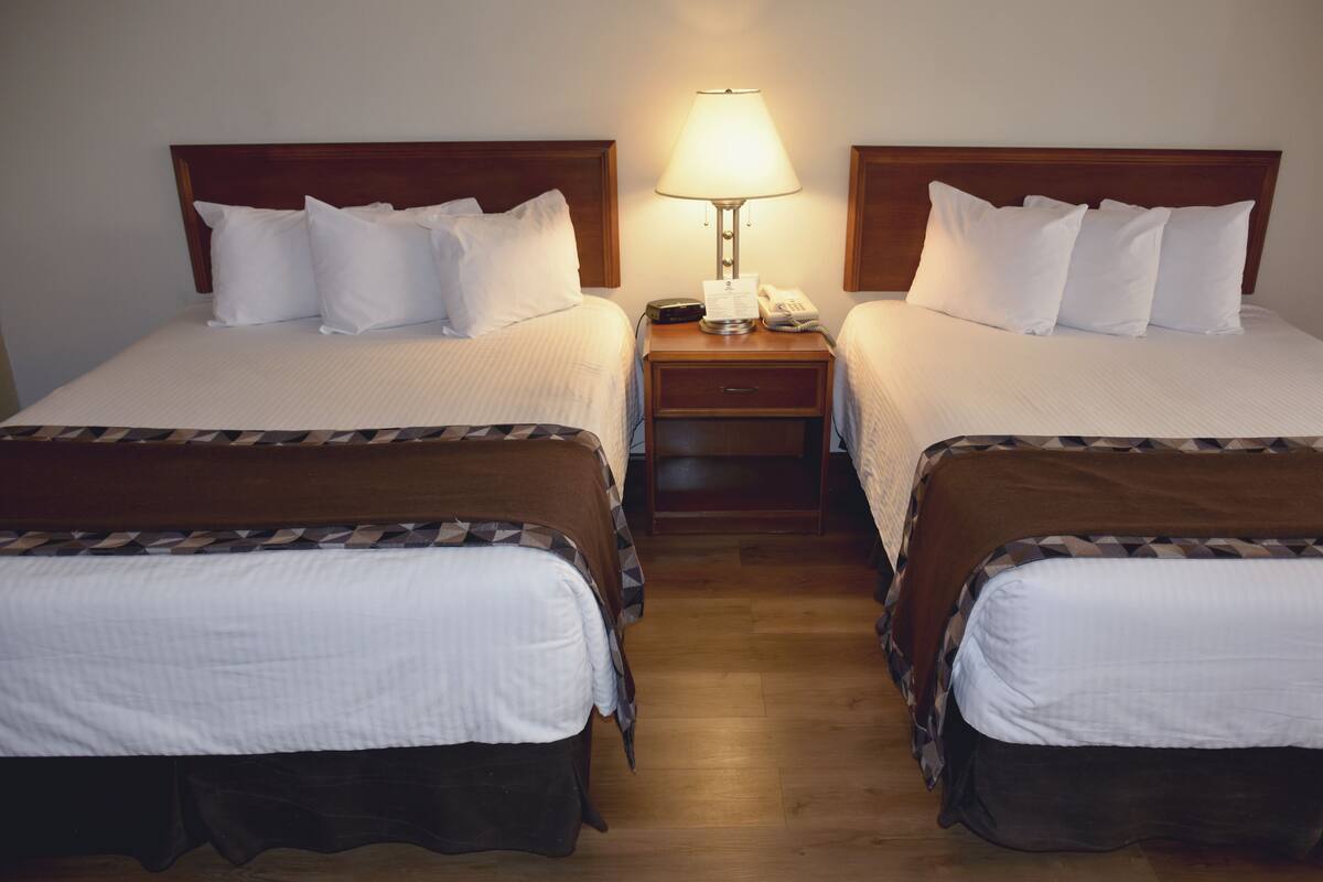 Ein Hotelzimmer mit zwei Einzelbetten, jeweils mit einem Holzkopfschild, einem Nachttisch mit Lampe und einem Telefon.