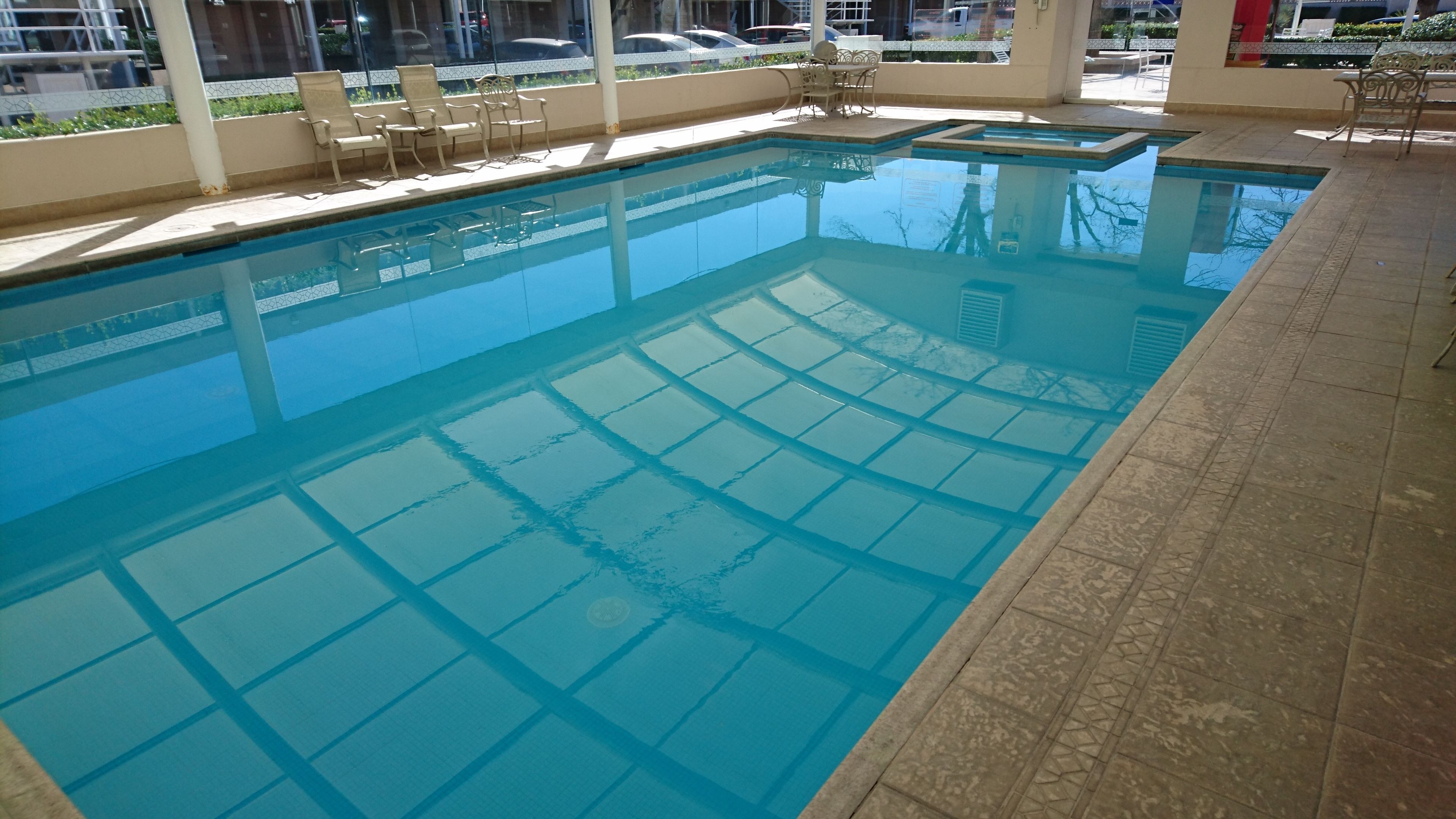 Una piscina interior cristalina con suelo de baldosas y techo de vidrio.