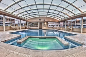An indoor swimming pool with a glass ceiling, surrounded by lounge chairs and a tiled floor. - HM Hotel Mirador (Chihuahua)