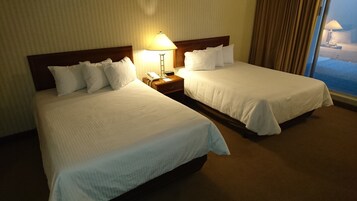 Two adjacent hotel beds with white linens, a bedside lamp, and a nightstand with a phone and notepad.