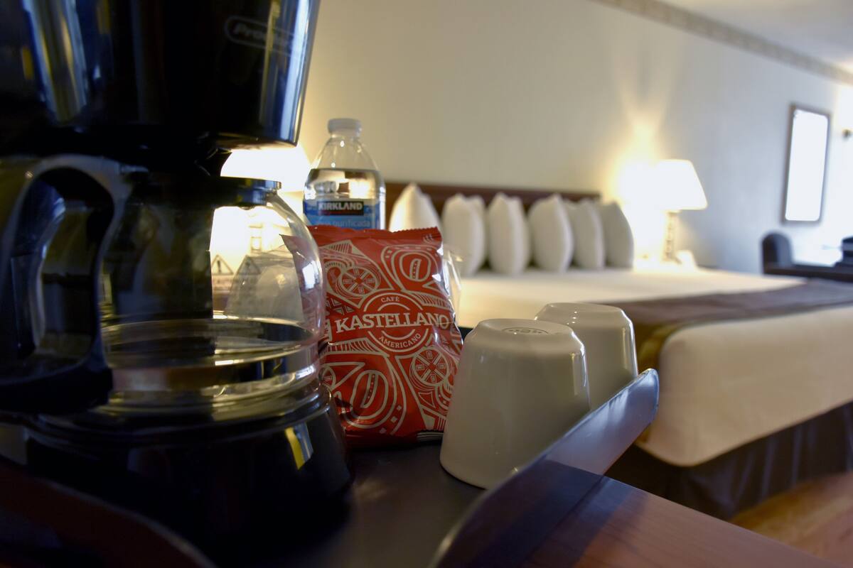 Ein Hotelzimmer mit einem Bett, einer Kaffeemaschine, einer Wasserflasche, einem Milchkännchen und einer Kaffeepackung.