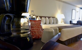 Habitación de hotel con cama, cafetera, botella de agua, jarra de leche y bolsa de café.