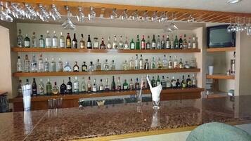 A bar area with multiple shelves of liquor bottles, a granite countertop, and hanging glassware.