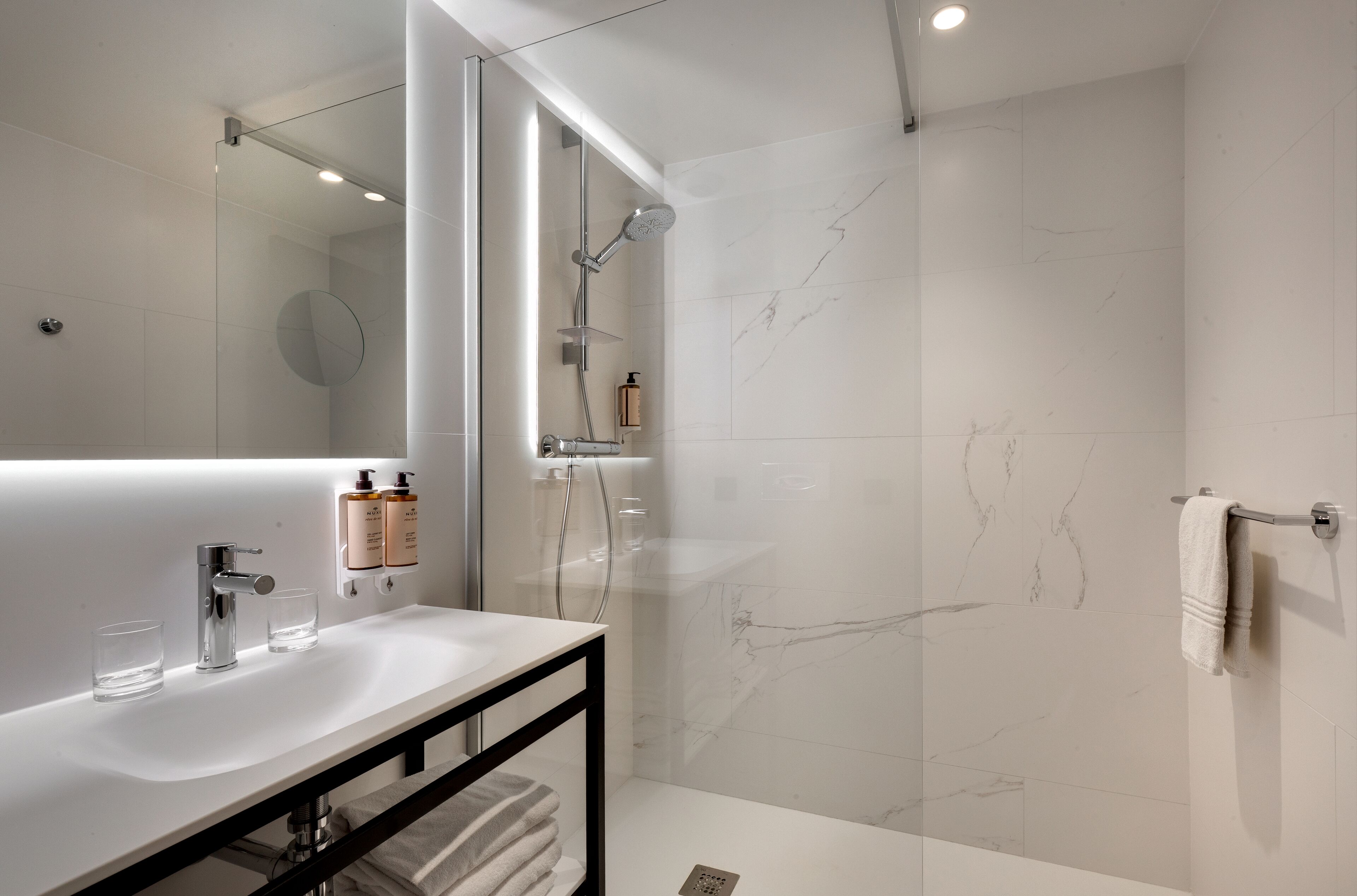 Un baño moderno con lavamanos, espejo y ducha blancos.