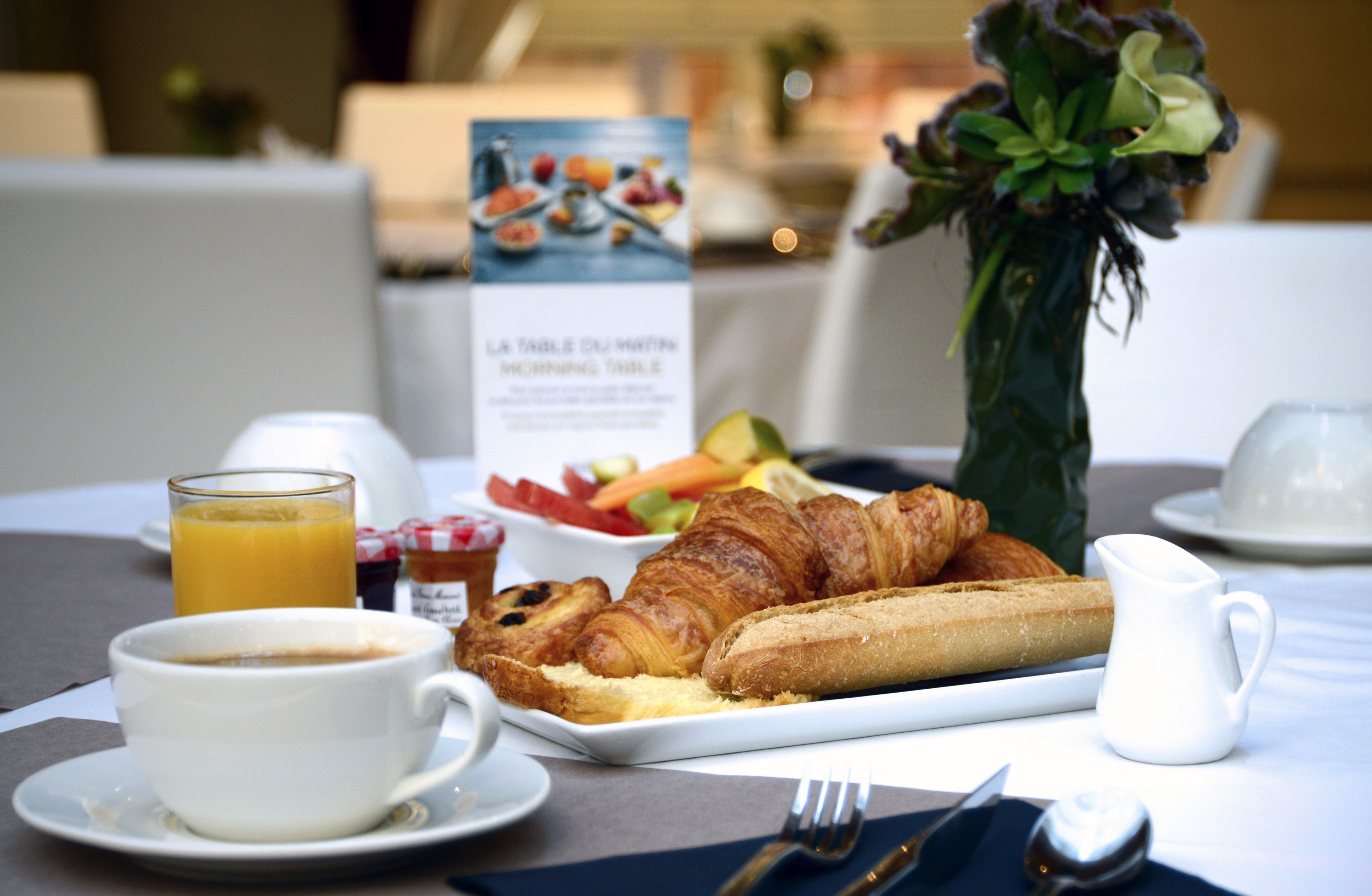 Ein Frühstückstisch mit Croissants, einem Croissant-Sandwich, einem Glas Orangensaft und einer kleinen Milchkanne.