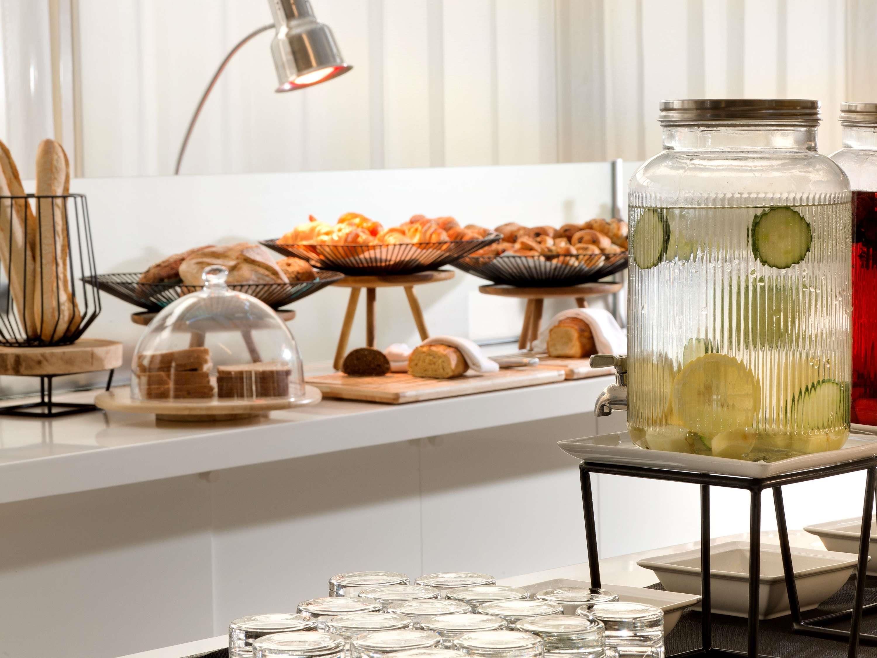 Montaje de bufé con diversas opciones de comida, incluyendo pan, pasteles y un tarro grande de pepinillos.