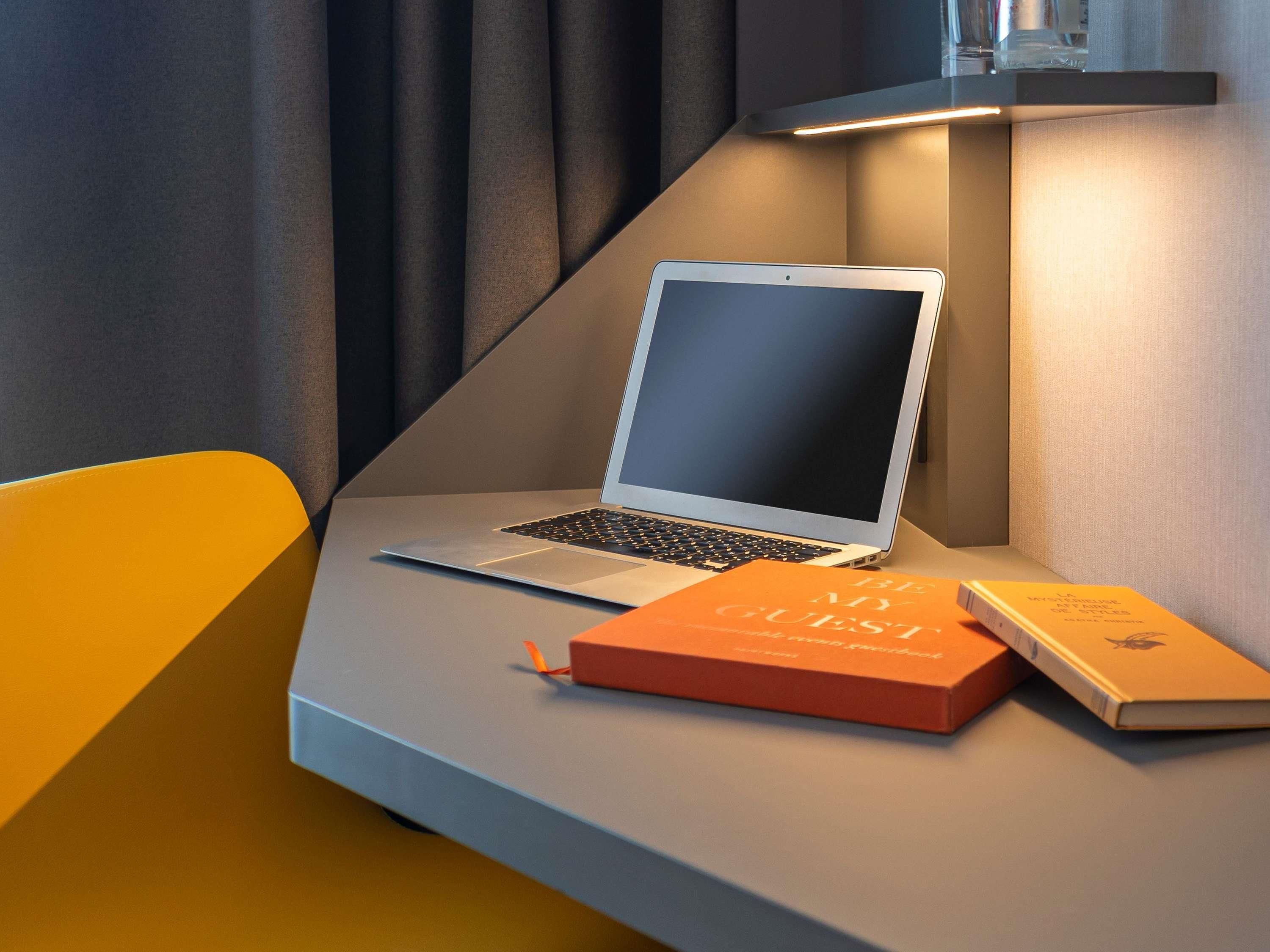 Un ordinateur portable sur un bureau, avec deux livres, une lampe et une chaise.