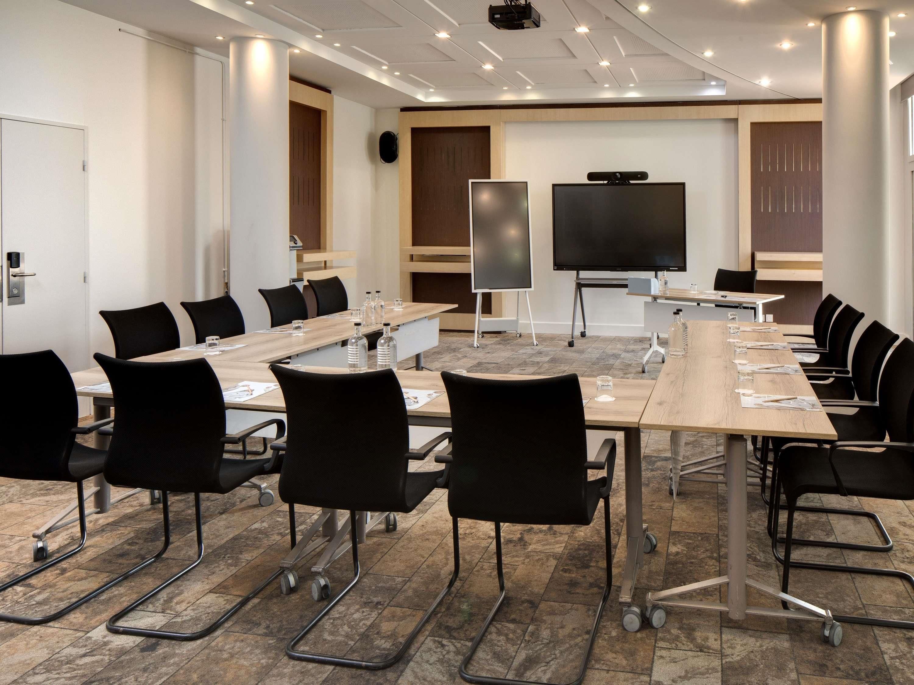 A conference room with a long table, black chairs, a projector screen, and a whiteboard.