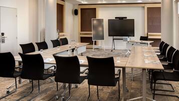 A conference room with a long table, black chairs, a projector screen, and a whiteboard.