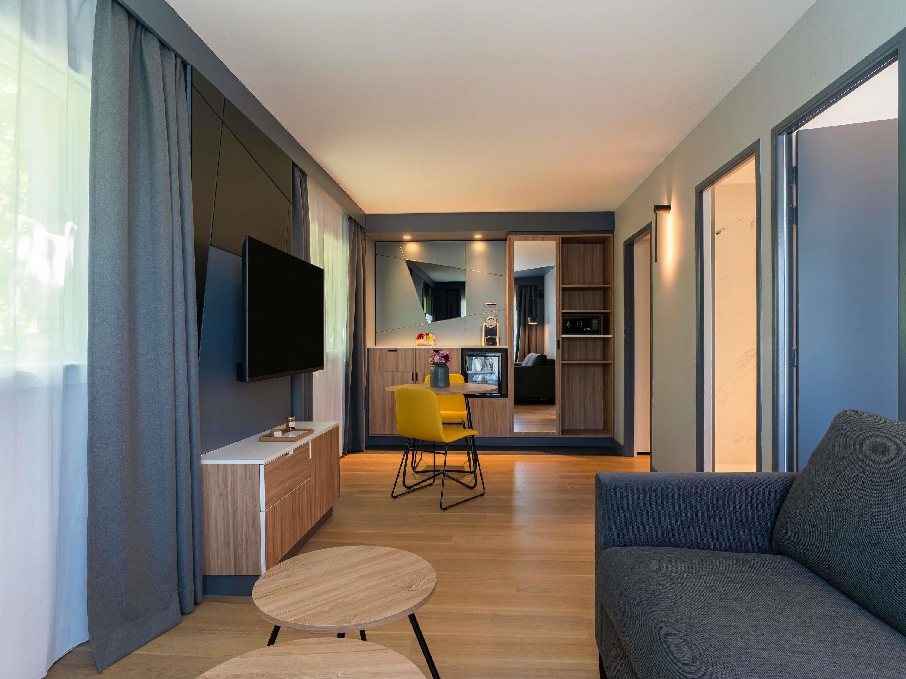 Un salon moderne doté d’un téléviseur à écran plat, d’un canapé, d’un coin repas avec une chaise jaune et d’un coin cuisine avec un four à micro-ondes.