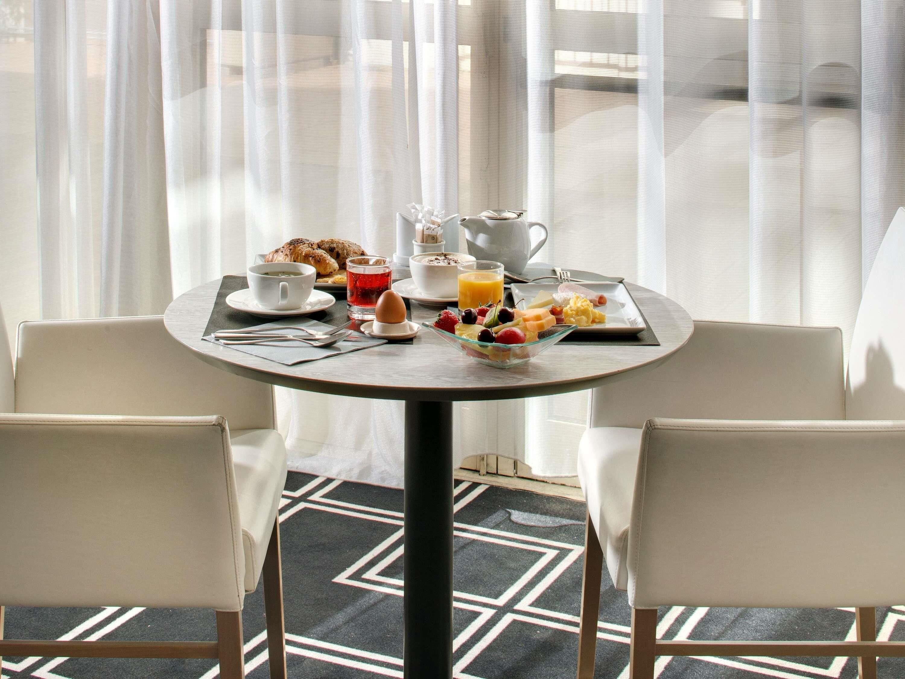 A breakfast table with a variety of food items, a teapot, and a cup of tea. There are two chairs around the table.