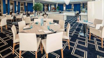 Un salón de conferencias de hotel con mesas redondas, sillas blancas y alfombra azul.