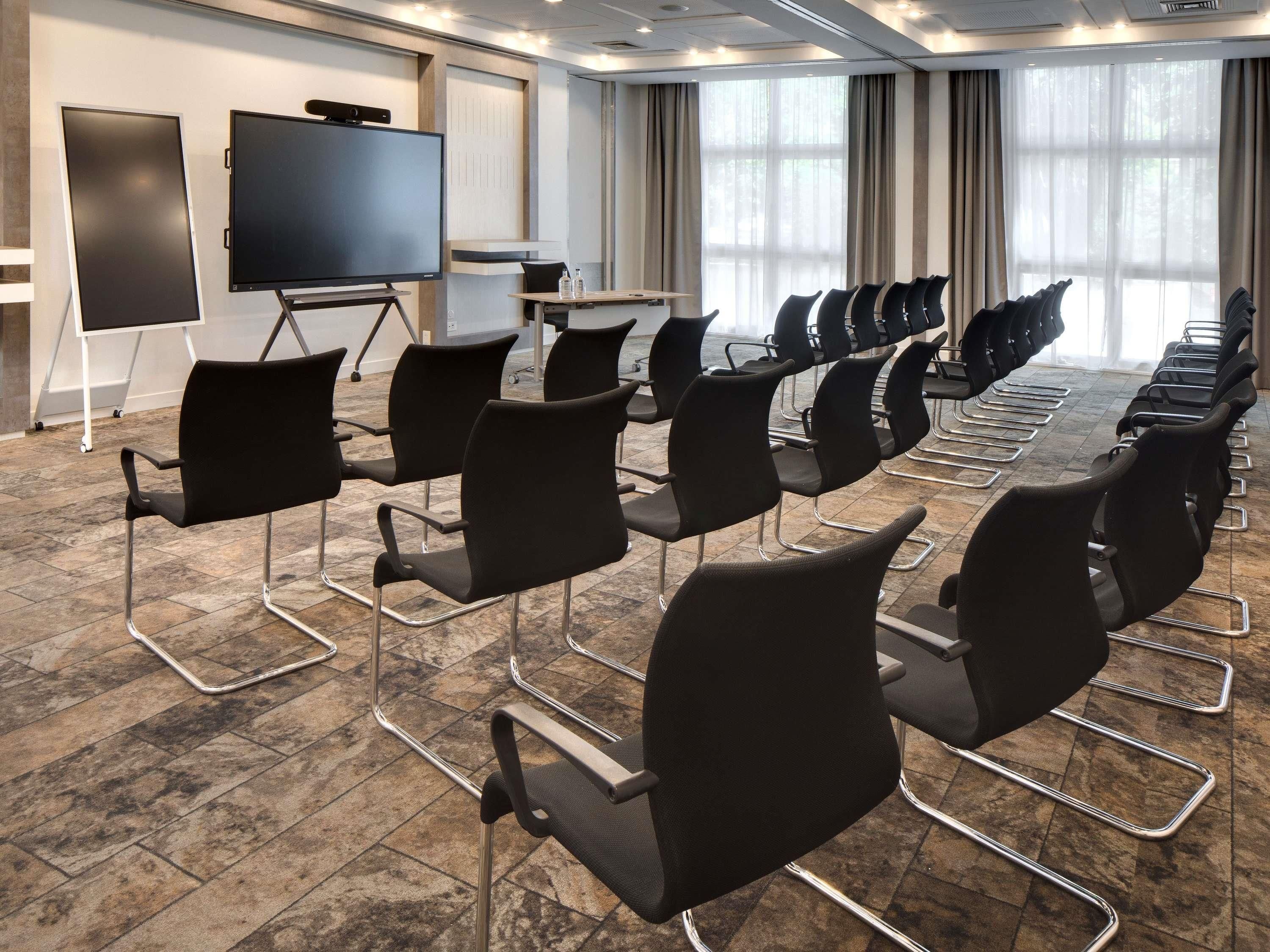 A conference room with rows of black chairs, a large flat-screen TV, and a presentation screen.