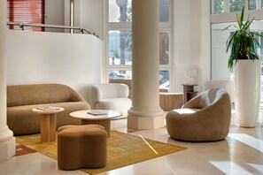 Un vestíbulo moderno con techo alto, una escalera y grandes ventanales.