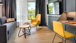 A modern living room with a grey sofa, yellow chairs, a small round table, and a TV mounted on the wall. - Mercure Montpellier Centre Antigone (Montpellier)