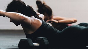 Deux personnes font de l'exercice avec des haltères dans une pièce dont les murs sont unis et le sol est en béton.