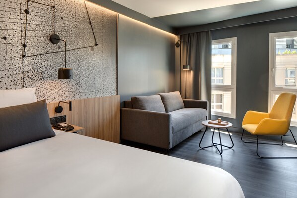 Una habitación de hotel moderna con una cama grande, un sofá, una mesita y un sillón amarillo.