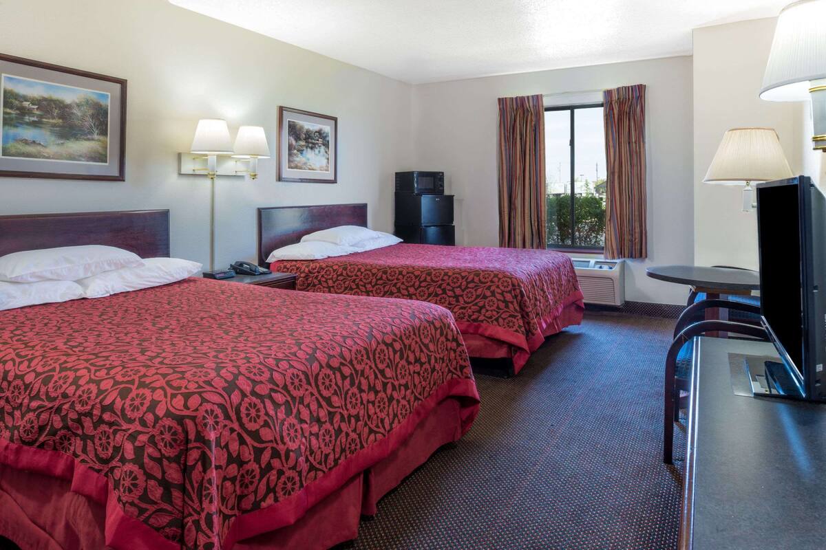 Camera d'albergo con due letti, una scrivania, una televisione e una finestra con tende.