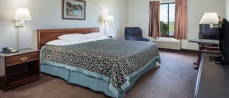 A hotel room with a large bed, two bedside lamps, a chair, a desk, and a TV.