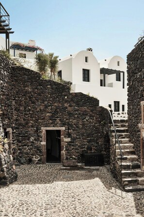 A stone-walled courtyard with a staircase leading to a white building with arched windows.