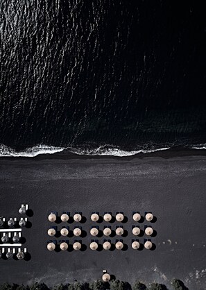 An aerial view of a beach with rows of sun umbrellas and lounge chairs.