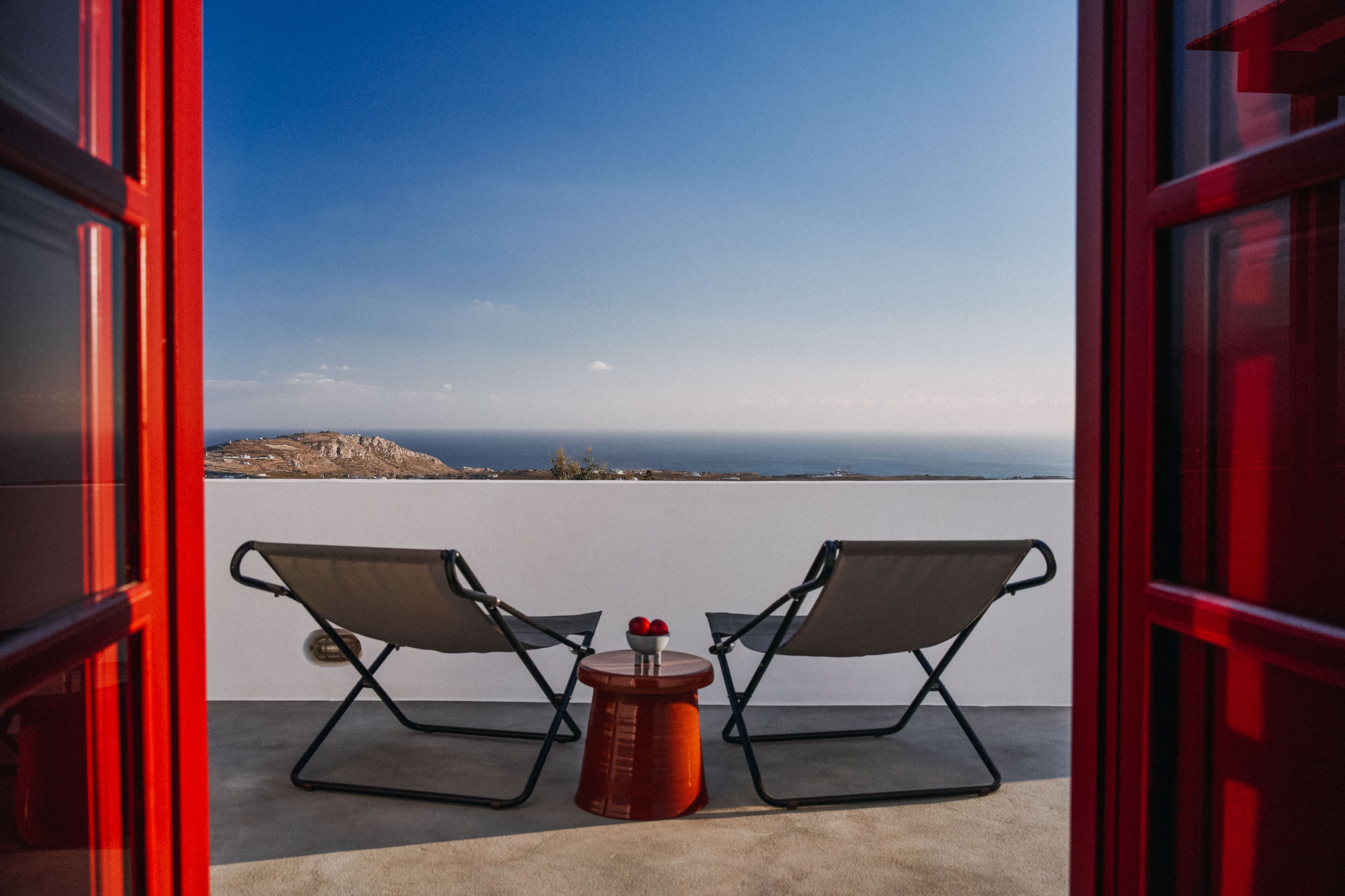 A balcony with two lounge chairs and a small table, overlooking a coastal landscape.