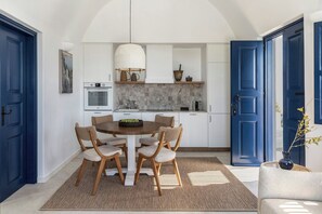 A dining area with a round table and six chairs, a kitchen with white cabinets and a blue door, and a living area with a sofa and a vase.