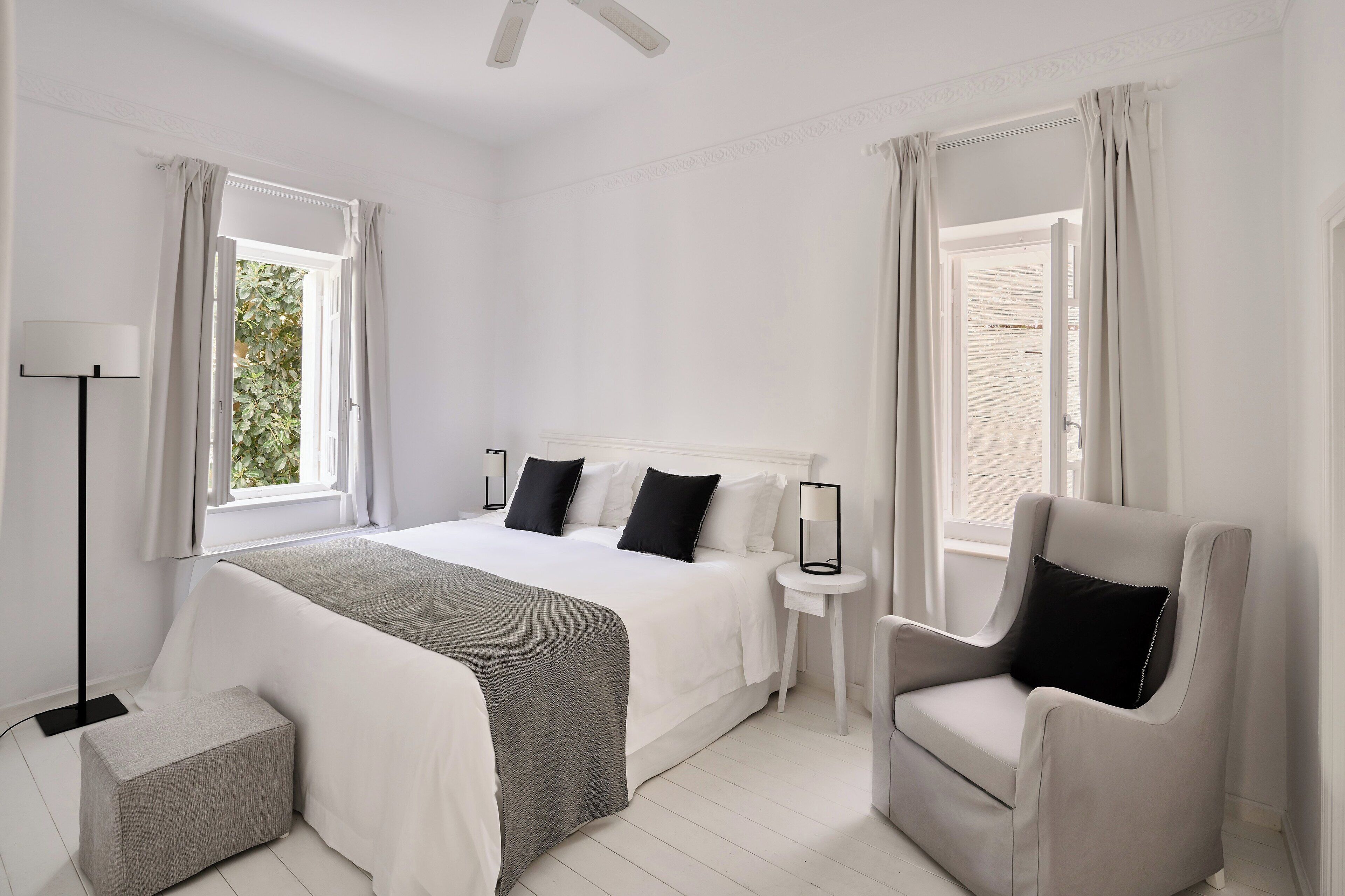 Quarto com cama, mesas de cabeceira, uma cadeira e janela com cortinas.