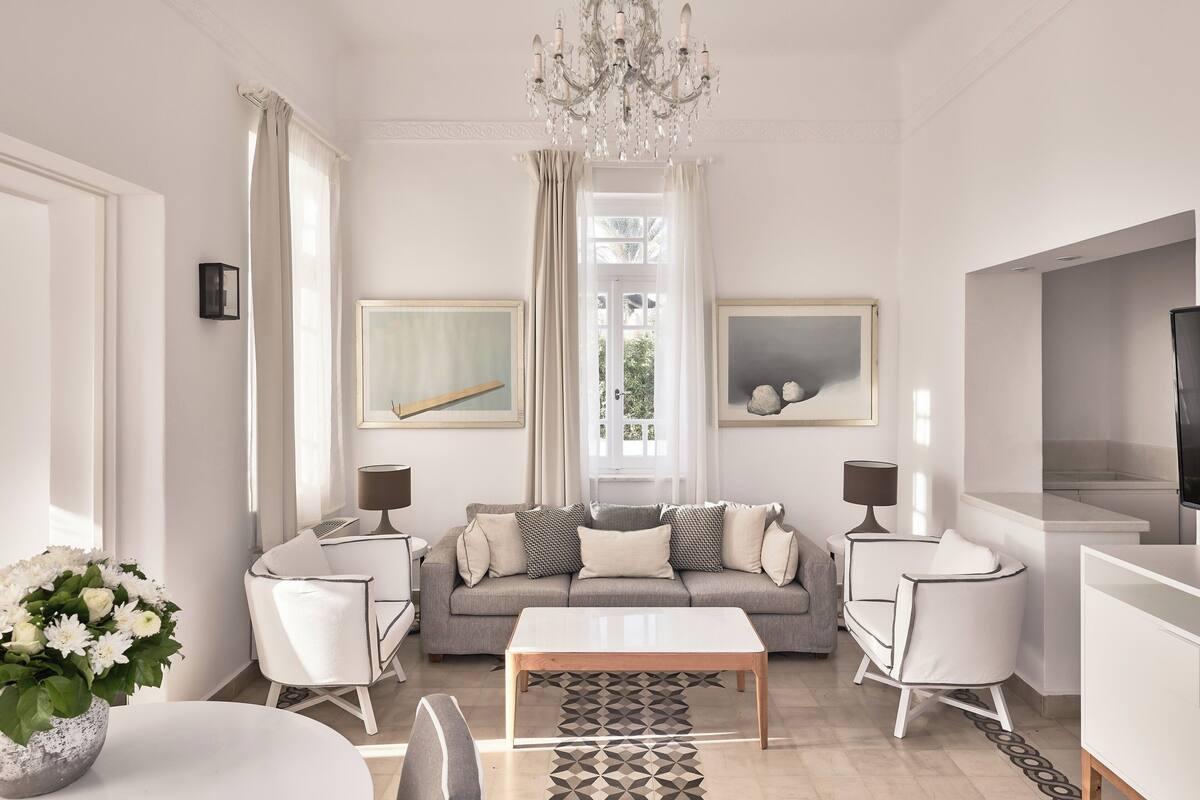 A modern living room with a grey sofa, white armchairs, a wooden coffee table, and a chandelier.